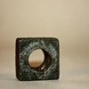 Close-up of a rustic square nut with a circular hole on a neutral background.